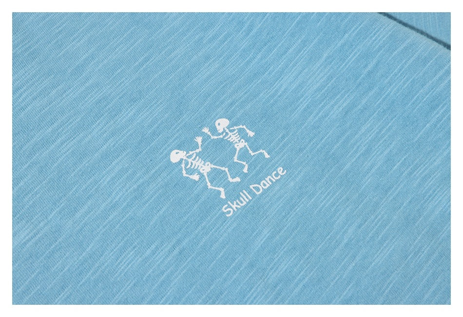White dancing skeletons and “Skull Dance” print on light blue shirt fabric.
