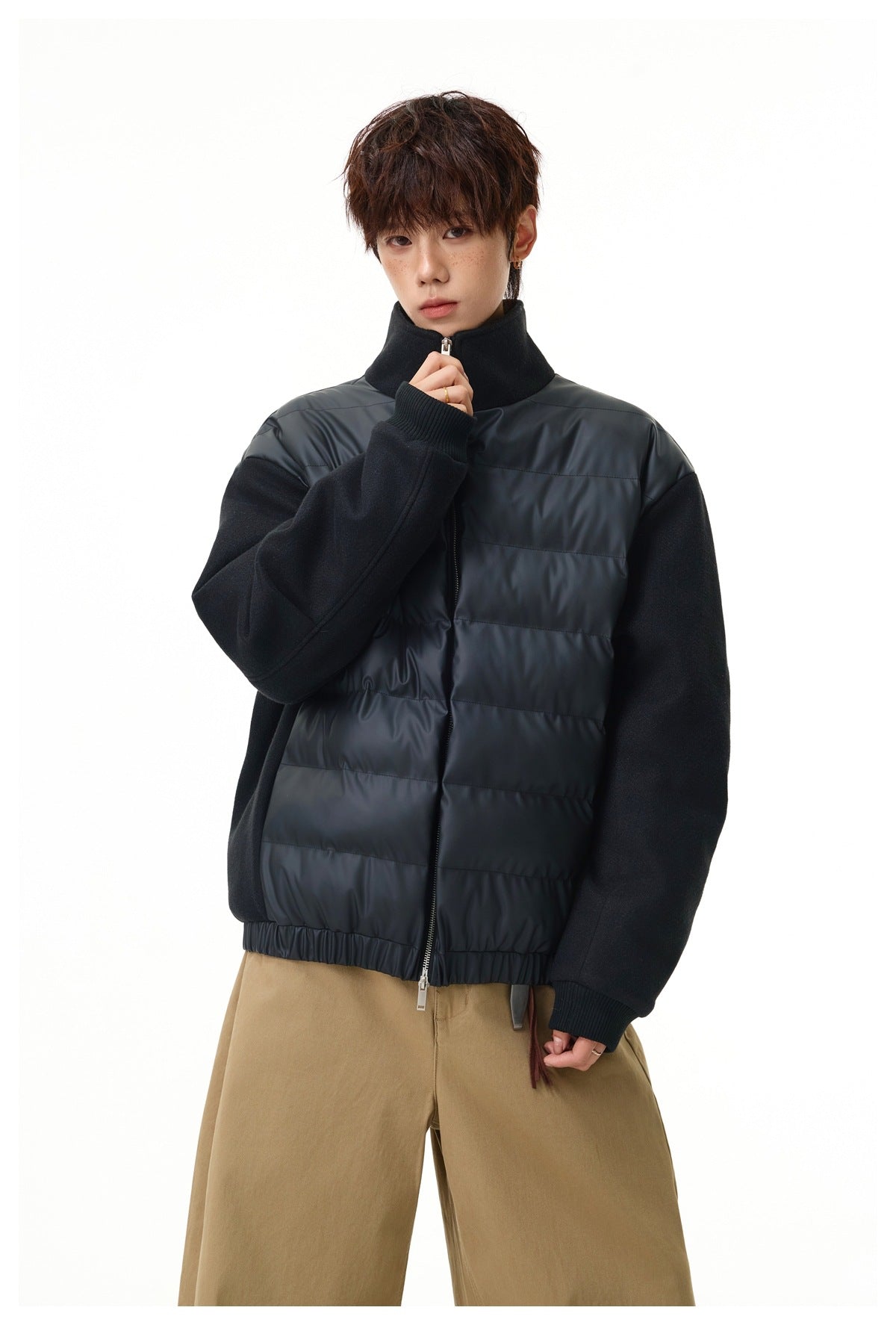 Model wearing black quilted-front stand-collar jacket with textured sleeves, zipped, with tan wide-leg pants