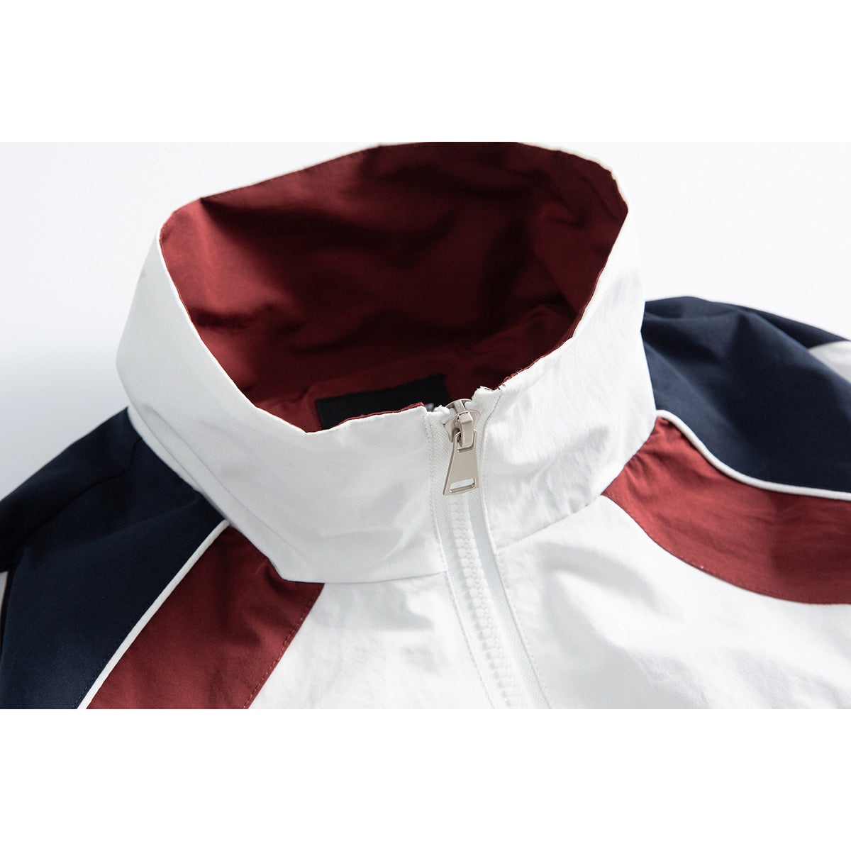 Close-up of a white track jacket collar with burgundy lining, navy shoulder panels and a front zipper.