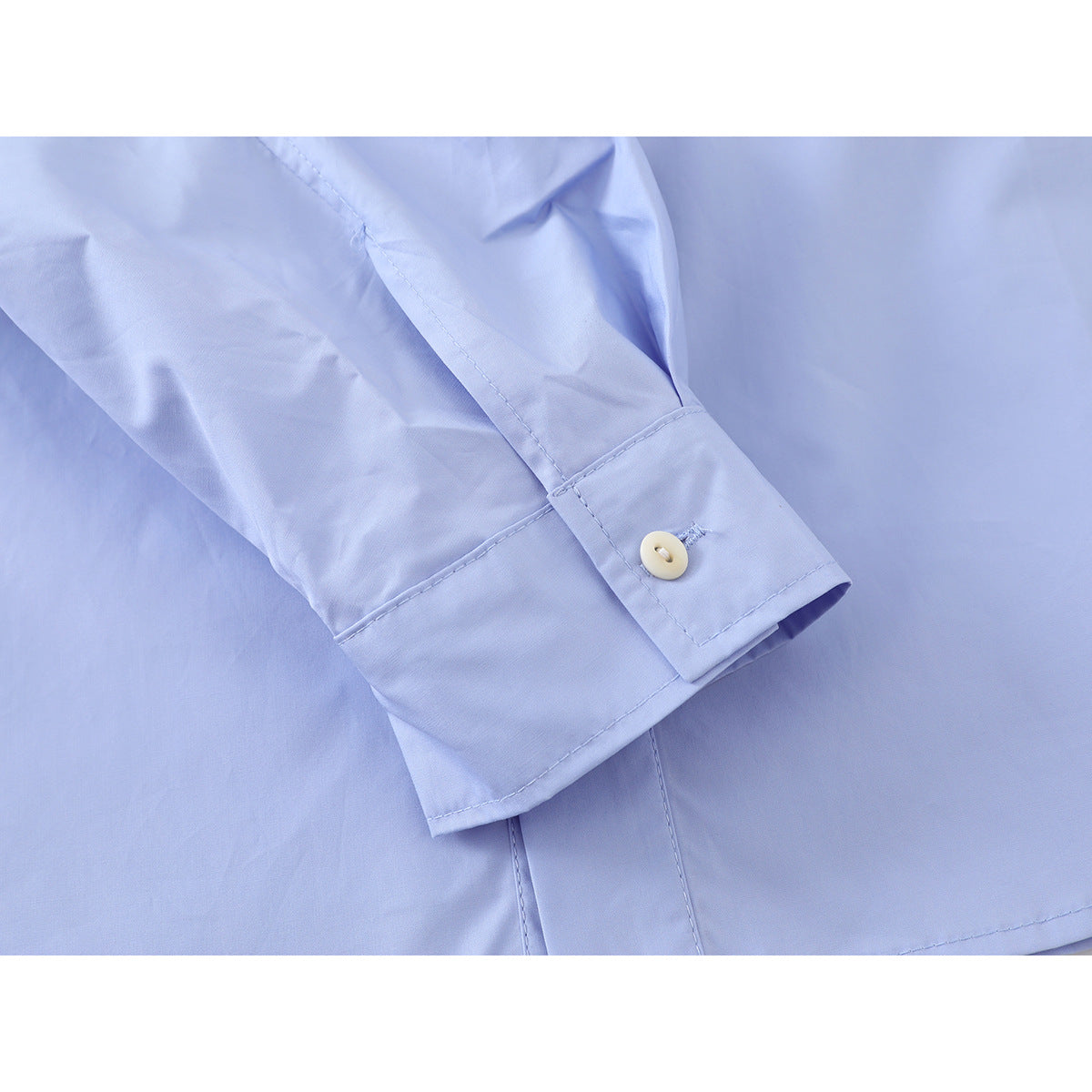 Close-up of a light blue shirt sleeve cuff with a button and visible stitching.