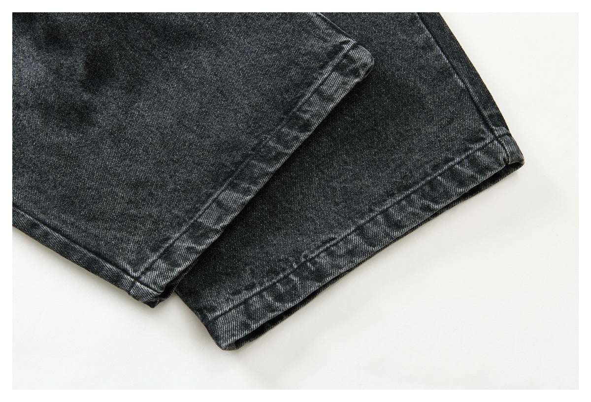 Close-up of the stitched hems of dark charcoal washed denim jeans.
