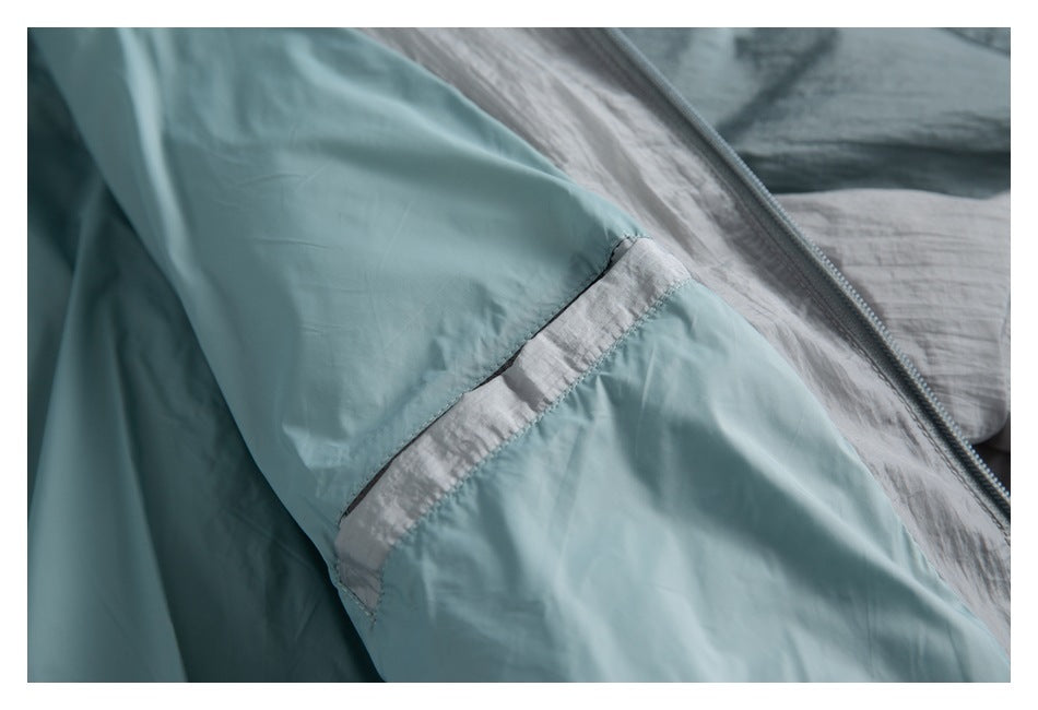 Close-up of a pale teal garment sleeve with a light gray panel and zipper edge.