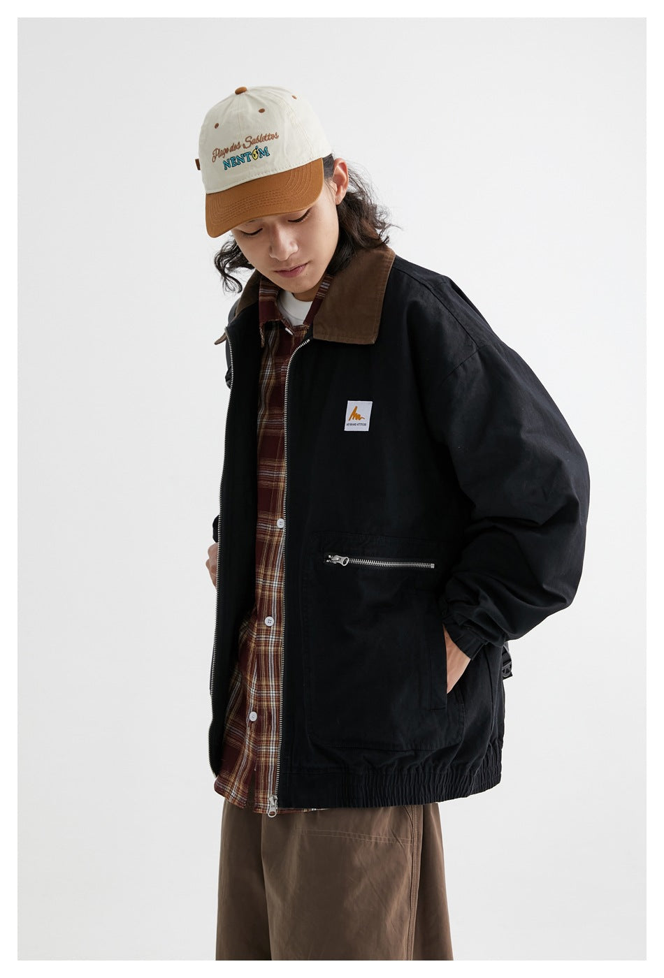 Angled view of a model wearing a black zip-front jacket with a brown collar and a brown plaid shirt.