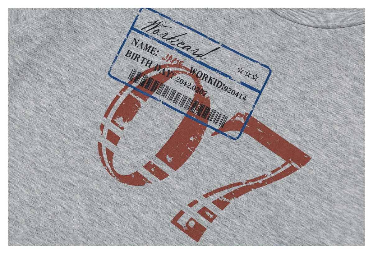 Close-up of a gray heather T-shirt print with a distressed red graphic, blue ID-style panel, lettering and barcode.
