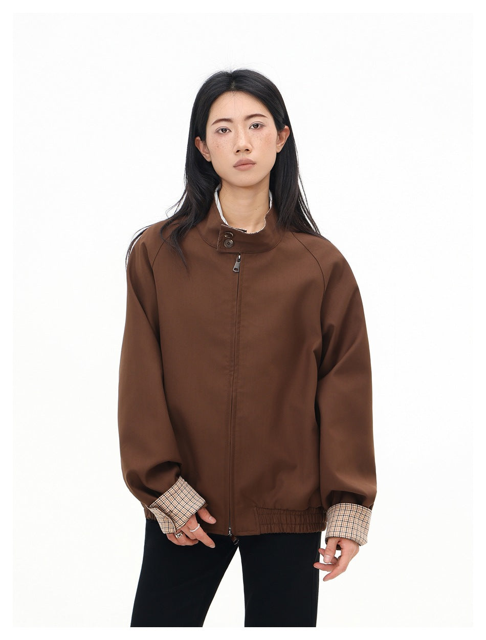Front view of a model wearing a brown jacket with a stand collar, center zipper, gathered hem, and checked cuffs.
