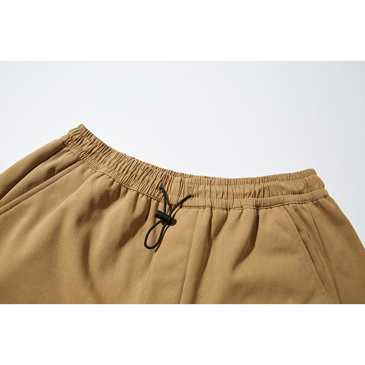 Close-up of tan jogger pants showing the elastic waistband, black drawcord and pocket seams.