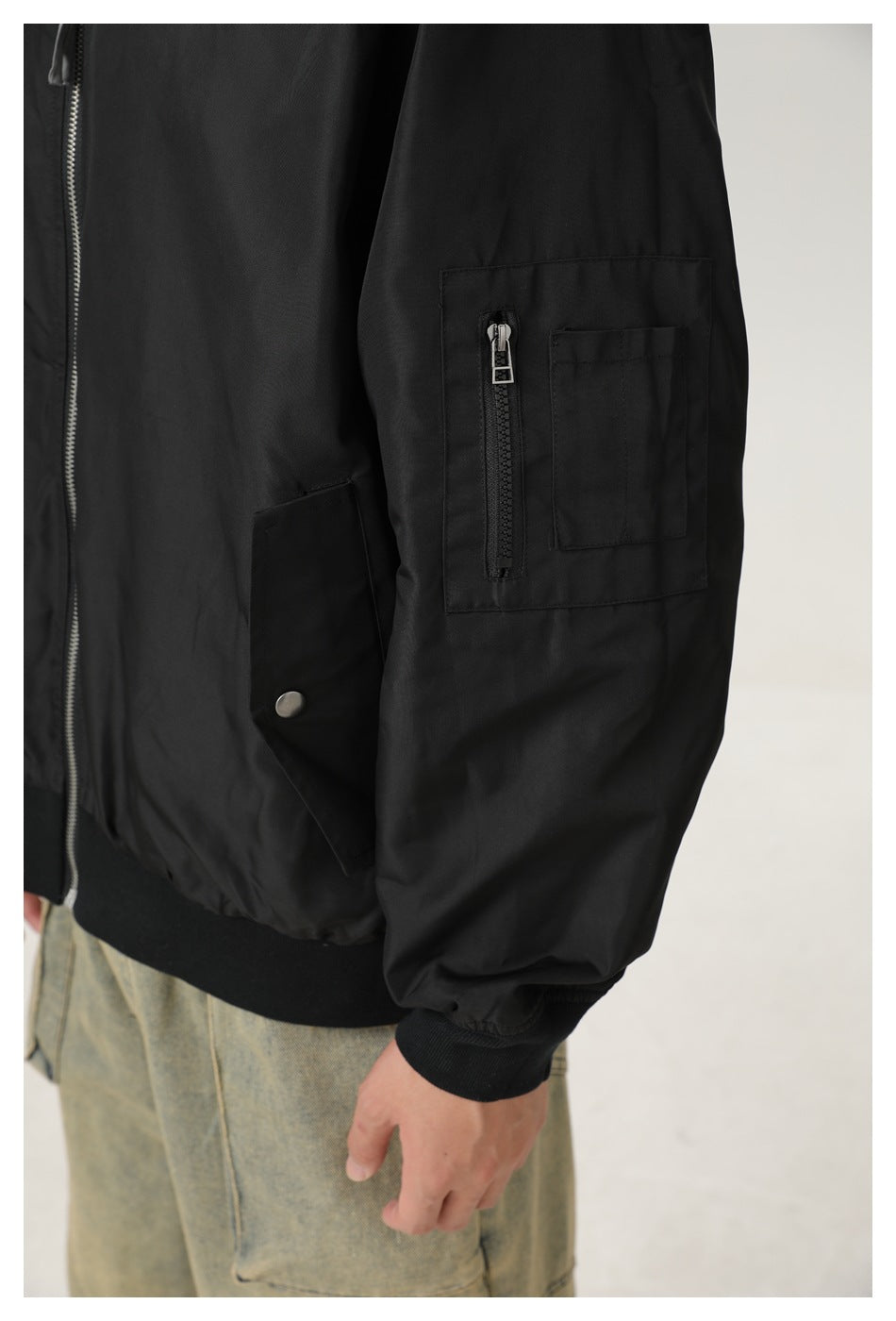 Close-up of the black bomber jacket's sleeve utility pocket, vertical zipper and front snap pocket.