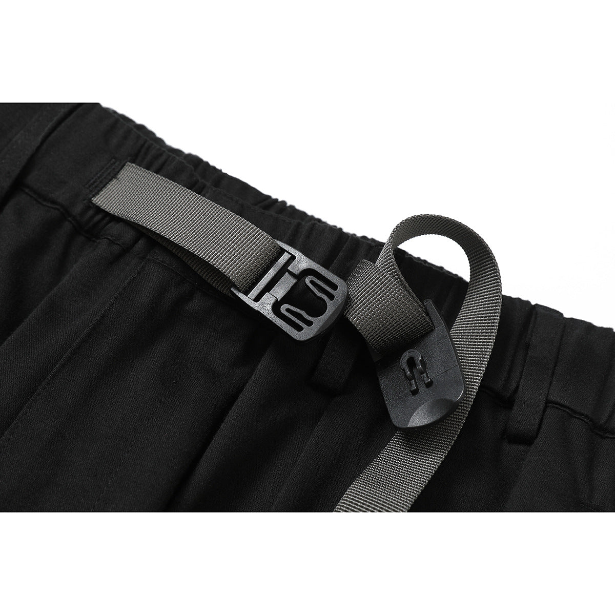 Close-up of black trousers showing an elastic waistband and a gray webbing belt with plastic hardware.