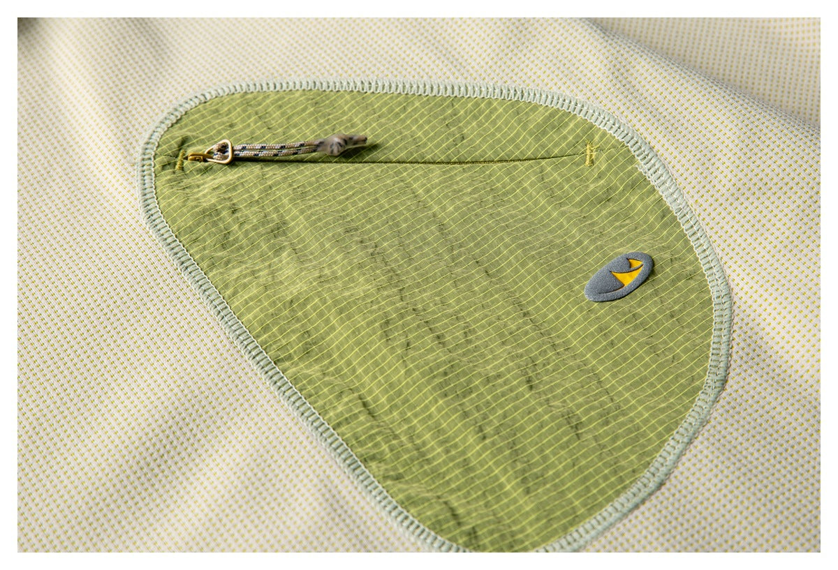 Close-up of an olive-green zip pocket with a small emblem on cream fabric dotted in yellow.