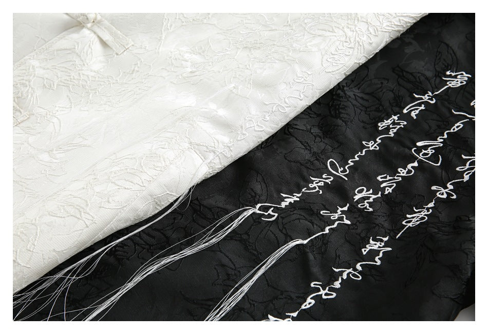 Close-up of ivory and black floral-patterned fabric with white cursive embroidery on the black garment.
