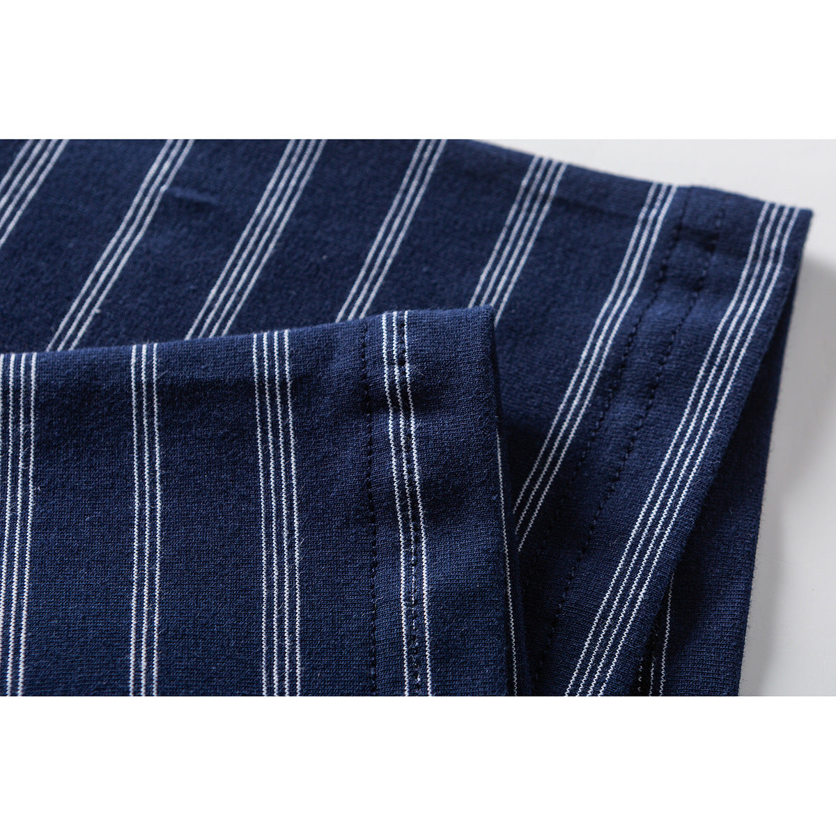 Close-up of the folded cuff and stitched hem on navy fabric with thin white stripes.