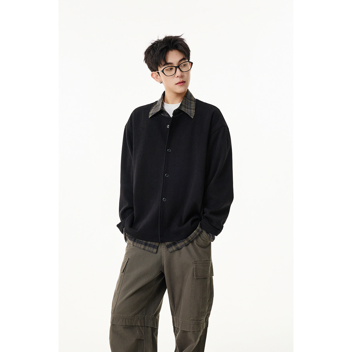 Front view of a model in a black button jacket with a plaid collar and hem, paired with cargo trousers.