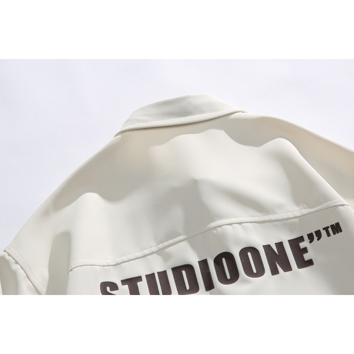 Close-up of the back of an ivory shirt, showing a large dark printed wordmark across the lower back.