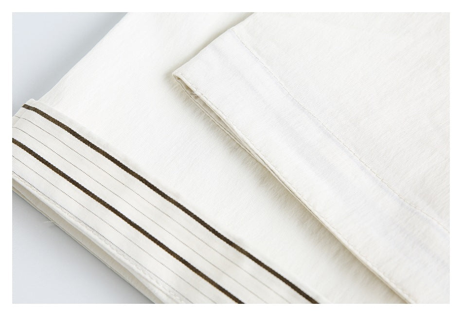 Close-up of an ivory garment edge with a folded panel and brown-striped trim.