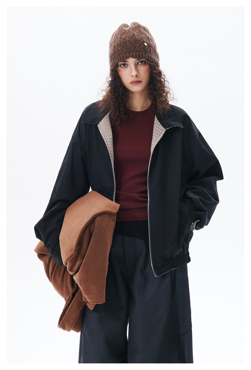 Front view of a model wearing a black zip jacket with checked lapel lining, burgundy top and brown knit beanie.