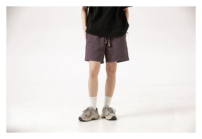 Cropped model wearing dark plum drawstring shorts, a black T-shirt, white socks and gray sneakers.