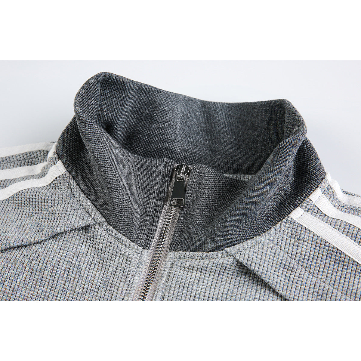 Close-up of a gray zip-up jacket's dark ribbed stand collar, front zipper, and white shoulder stripes.