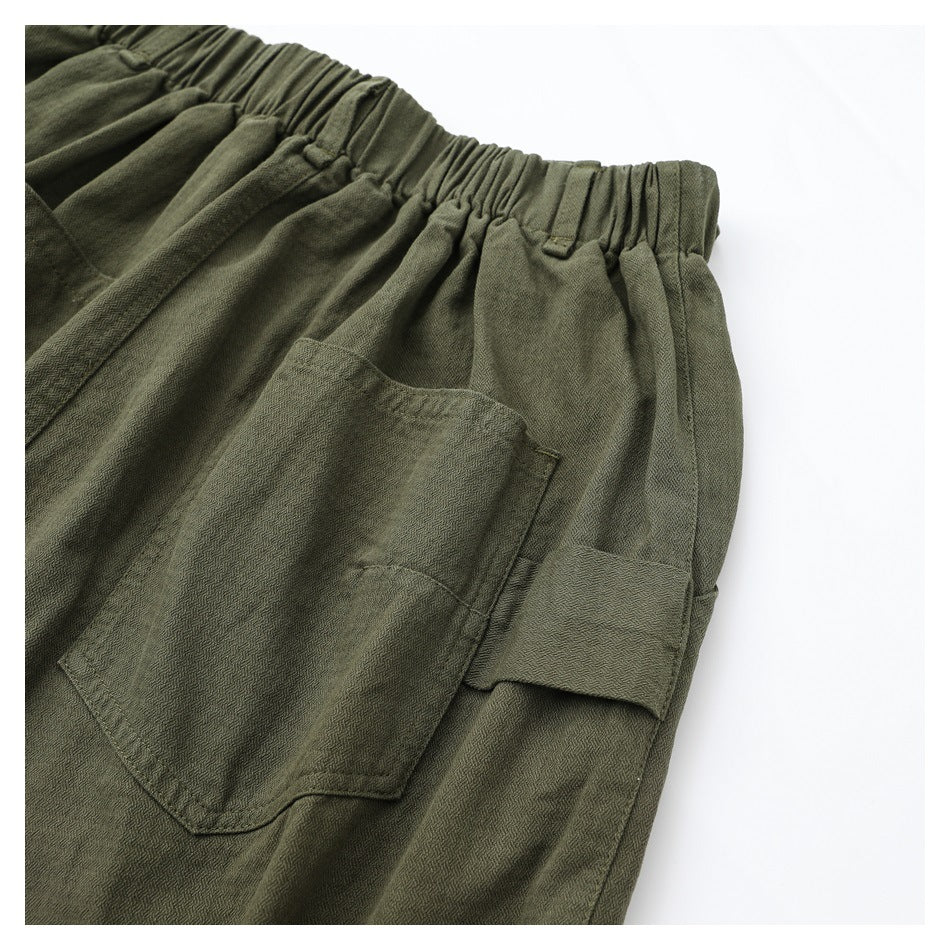 Close-up of olive-green trousers showing the elastic waistband and layered side pockets.