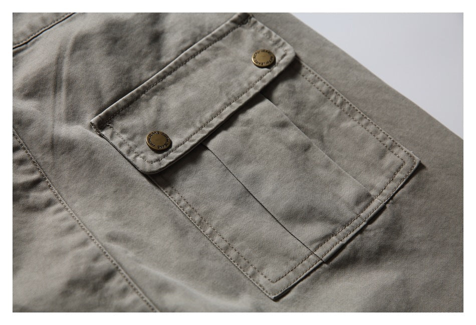 Close-up of a large stitched trouser pocket with a buttoned flap on taupe-gray fabric.