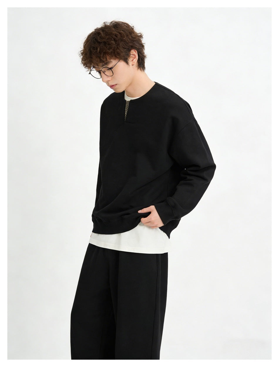 Person wearing black sweatshirt with checked neckline insert over a white tee and black wide-leg pants
