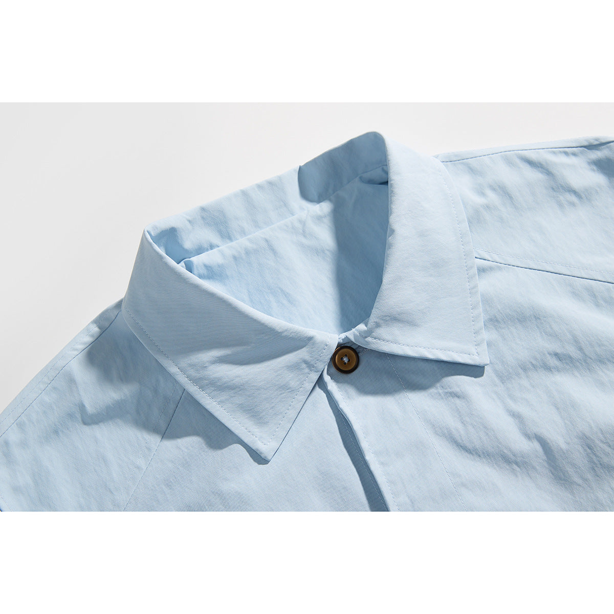 Close-up of a light blue shirt’s pointed collar, front placket, and brown button.