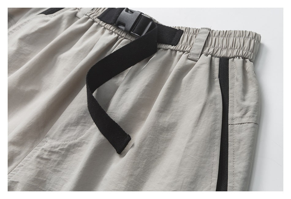 Close-up of light gray shorts showing a black buckle belt and vertical black-trimmed pocket.