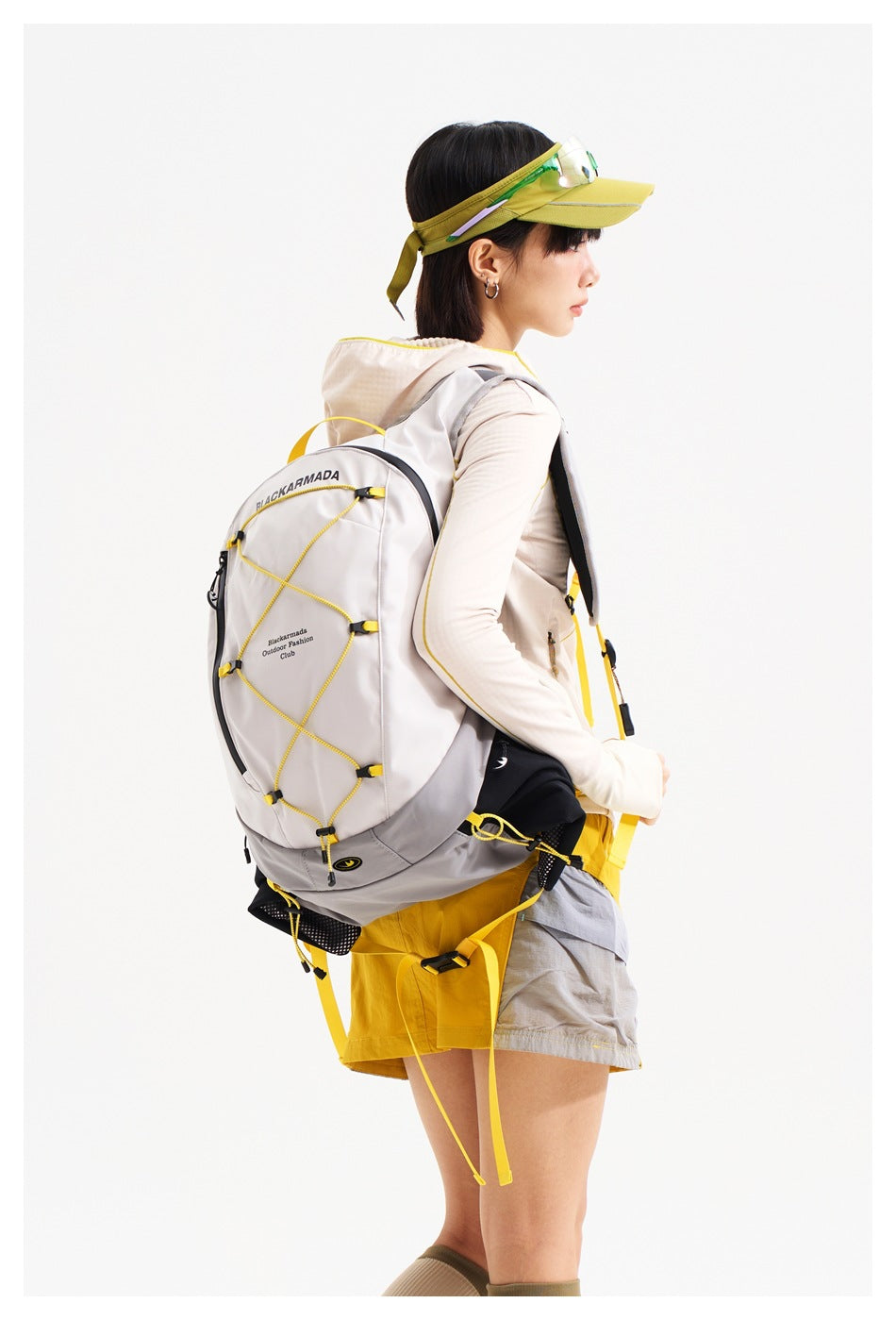 Side and rear view of a model wearing a gray backpack with yellow cord lacing and a yellow and gray outdoor outfit.