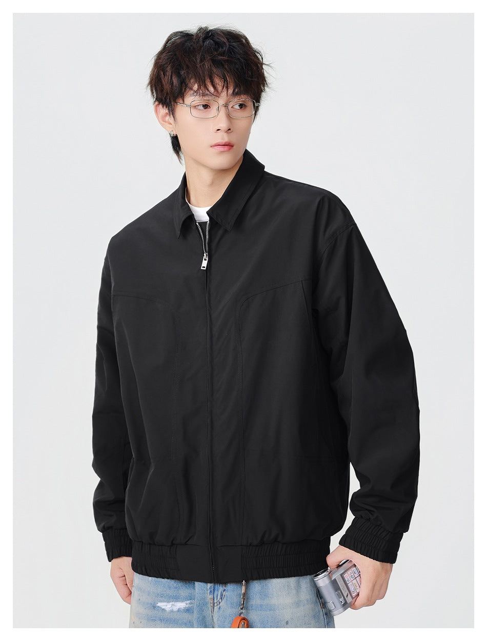 Model wearing a black collared zip jacket with elastic cuffs and hem, holding a small camera.