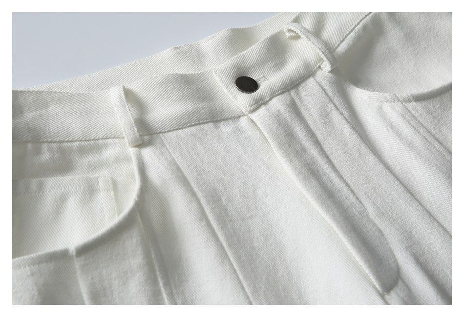 Close-up of white trousers showing the waistband, belt loop, dark button, and front pleats.