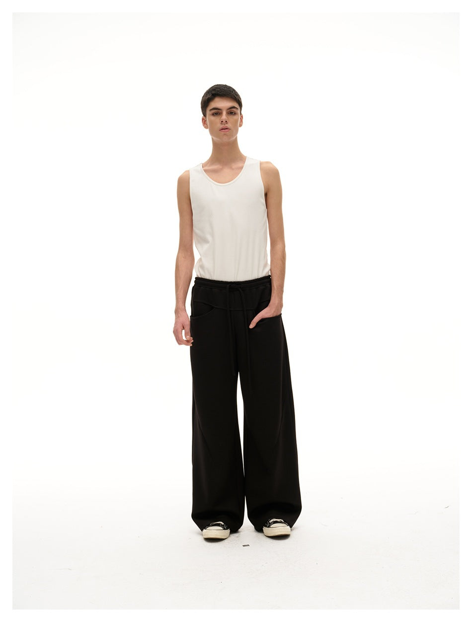 Front view of a model wearing black wide-leg drawstring pants with a white tank top.