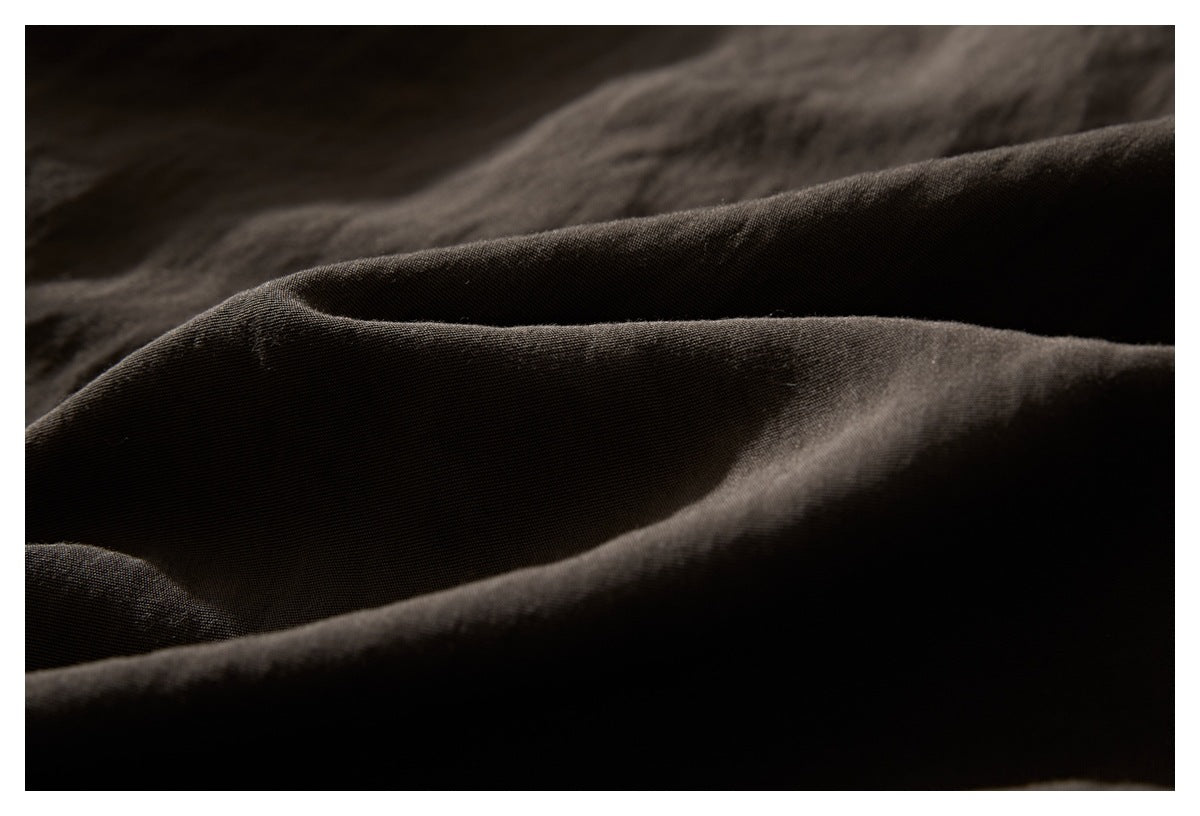 Macro view of dark brown shirt fabric gathered into soft folds, showing its surface texture.