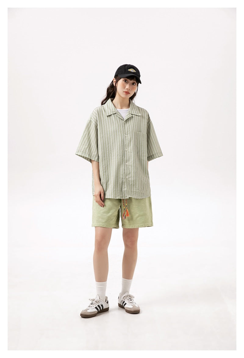 Model wearing light green shorts with a striped button-up shirt, white socks and sneakers.
