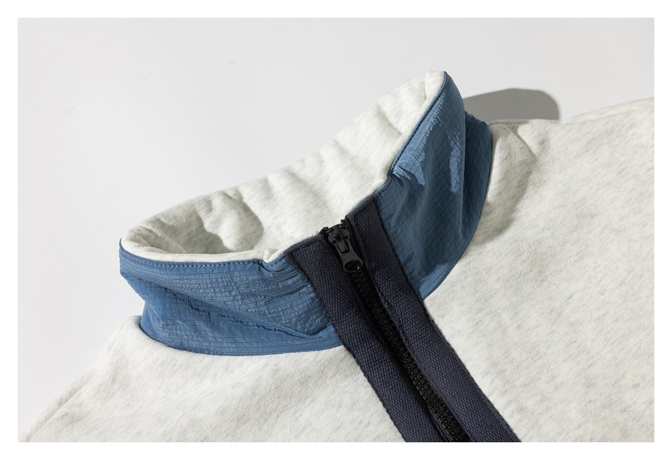 Close-up of a light gray pullover's blue stand collar and dark quarter zipper.
