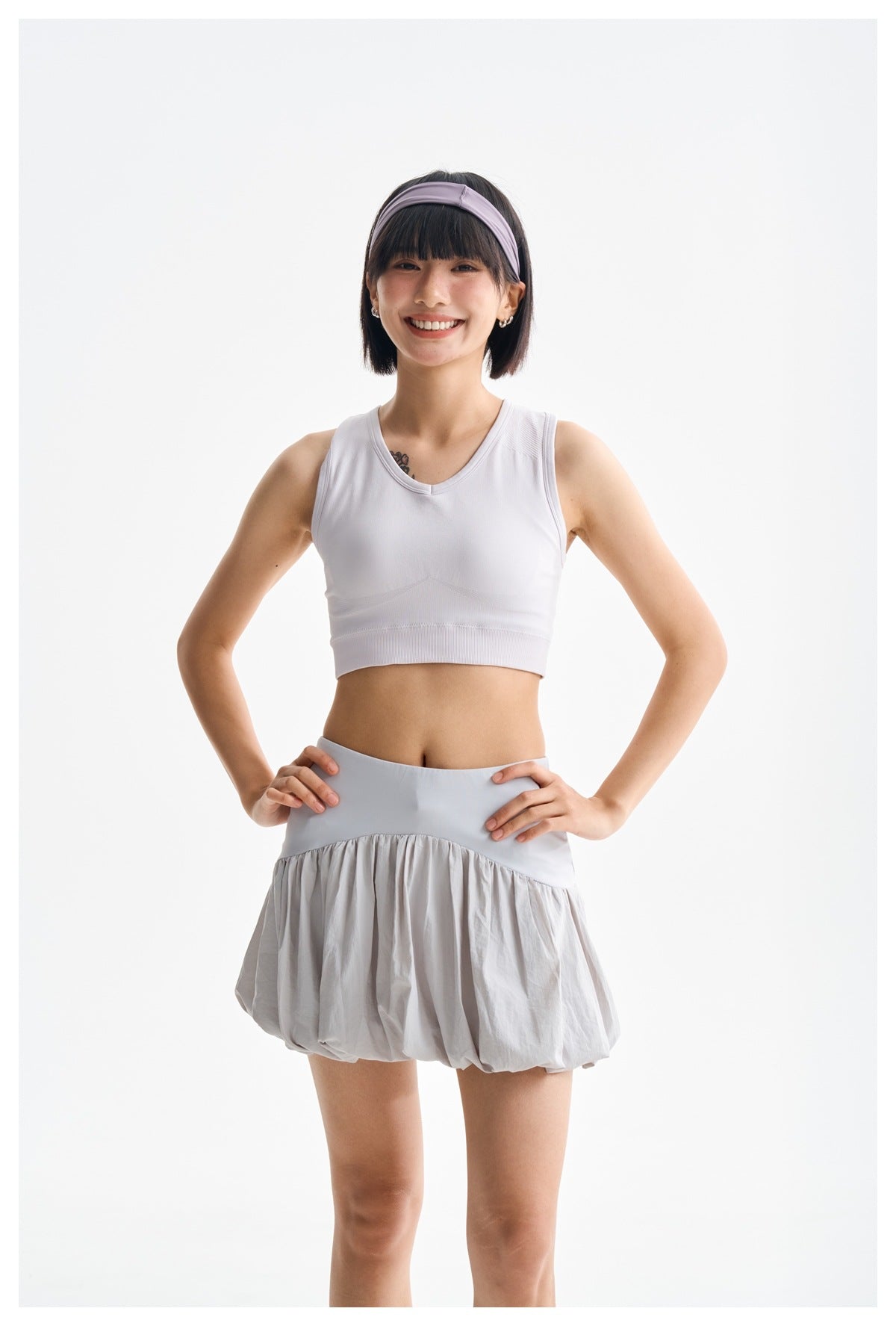 Model wearing a light gray bubble-hem skirt and white cropped athletic top, front view.