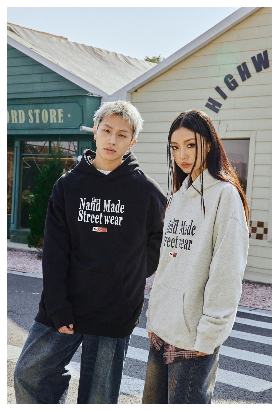 Two models pose in black and light gray pullover hoodies with large chest lettering and kangaroo pockets.
