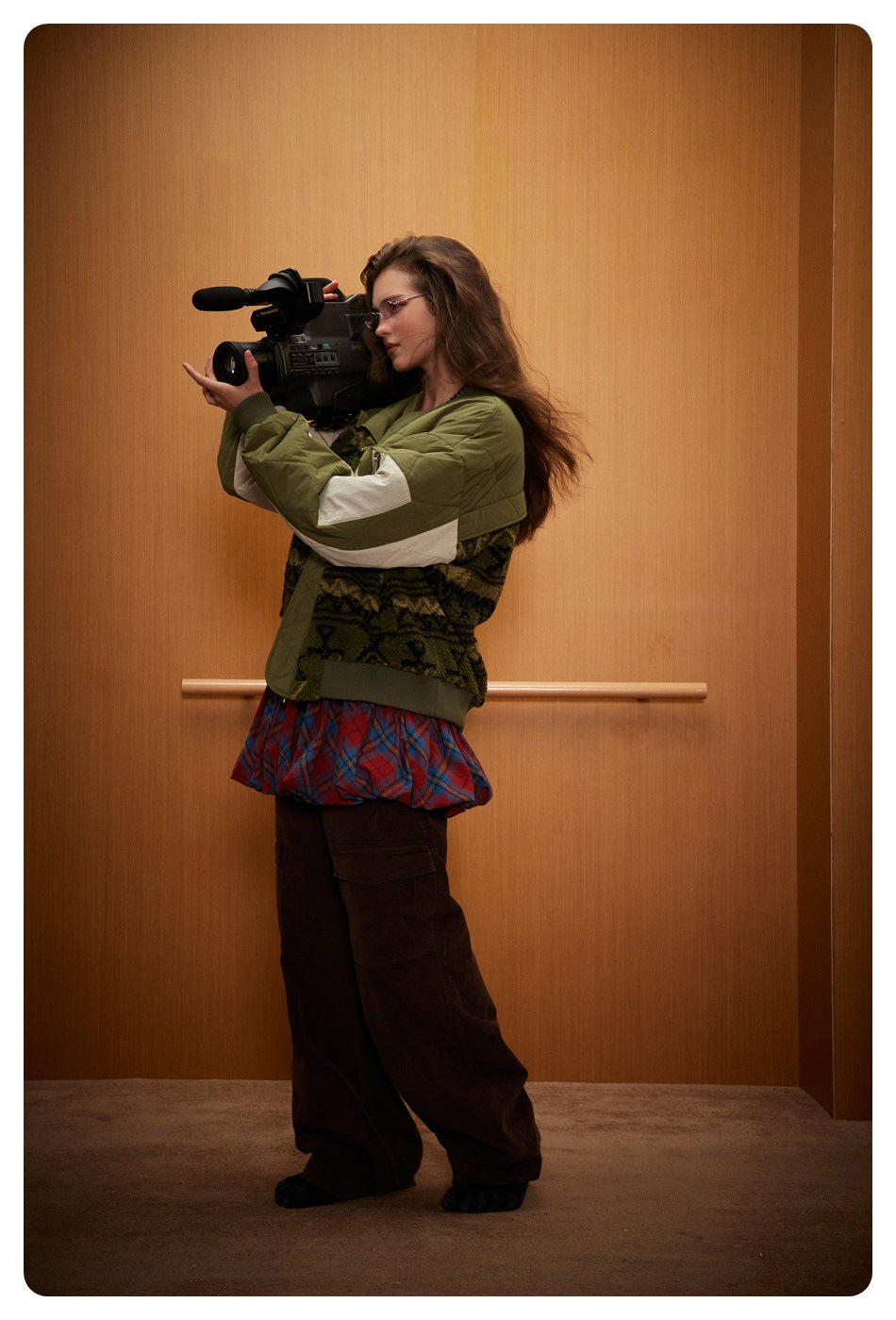 Side view of a model holding a video camera while wearing the olive quilted jacket with cream sleeve panels