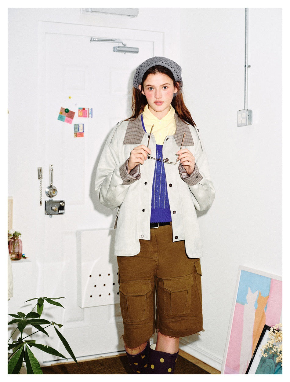 Model facing forward in the light gray jacket with plaid collar and cuffs, holding glasses, with brown cargo shorts