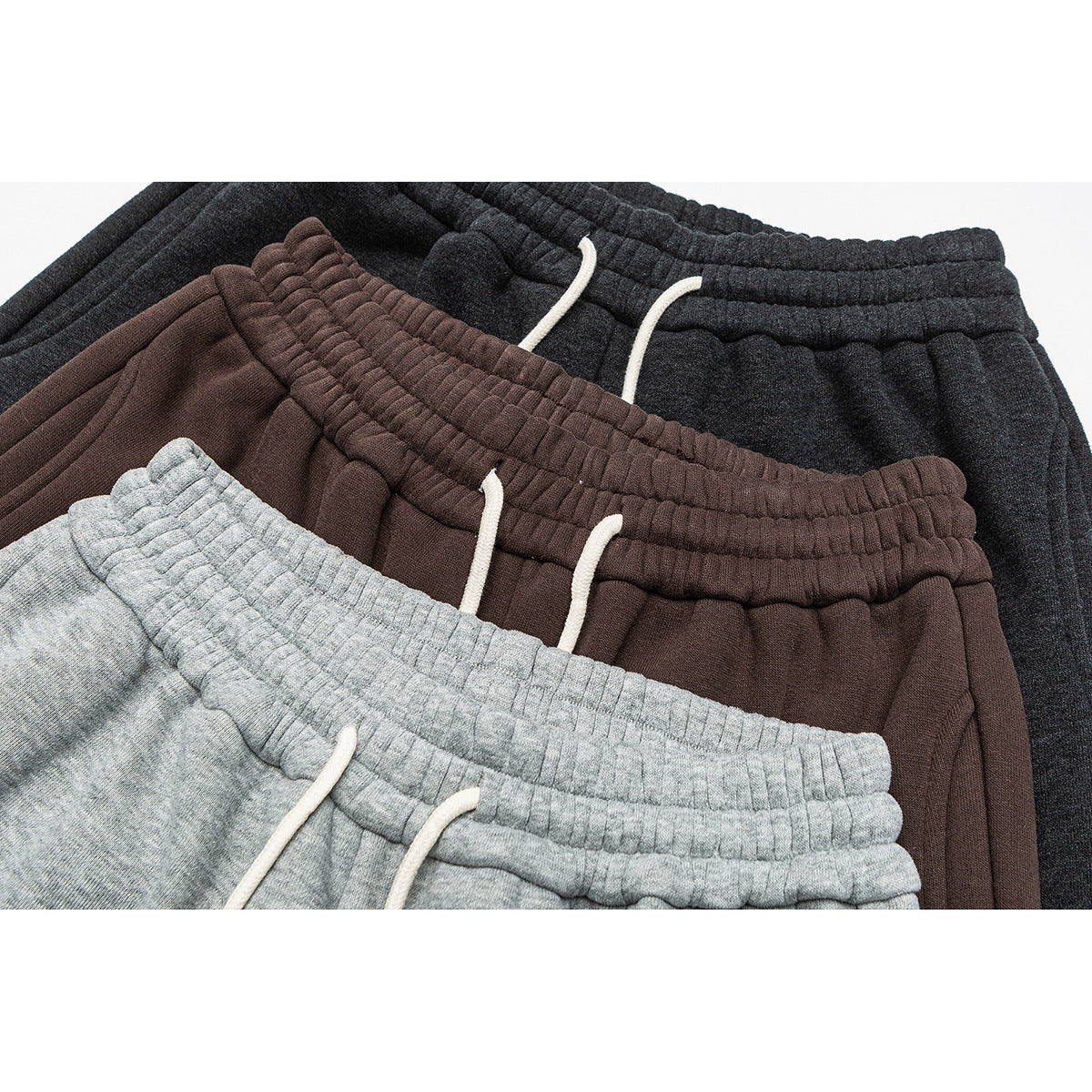 Close-up of light gray, brown, and charcoal jogger waistbands with white drawstrings.