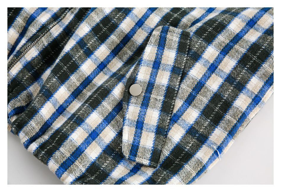 Close-up of a snap-button pocket flap on a blue, cream and dark green plaid jacket.