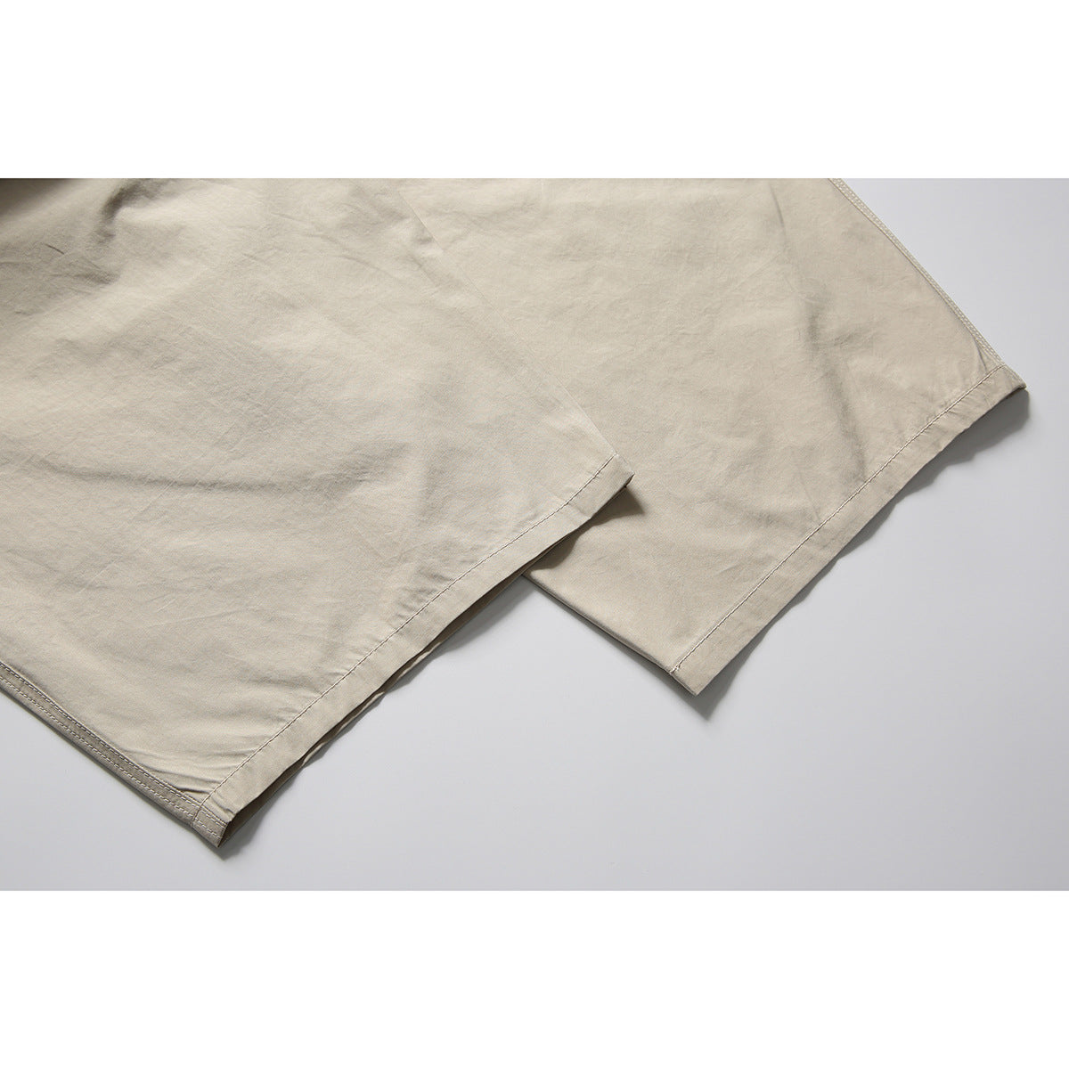 Close-up of the stitched hems of light beige pants laid flat.