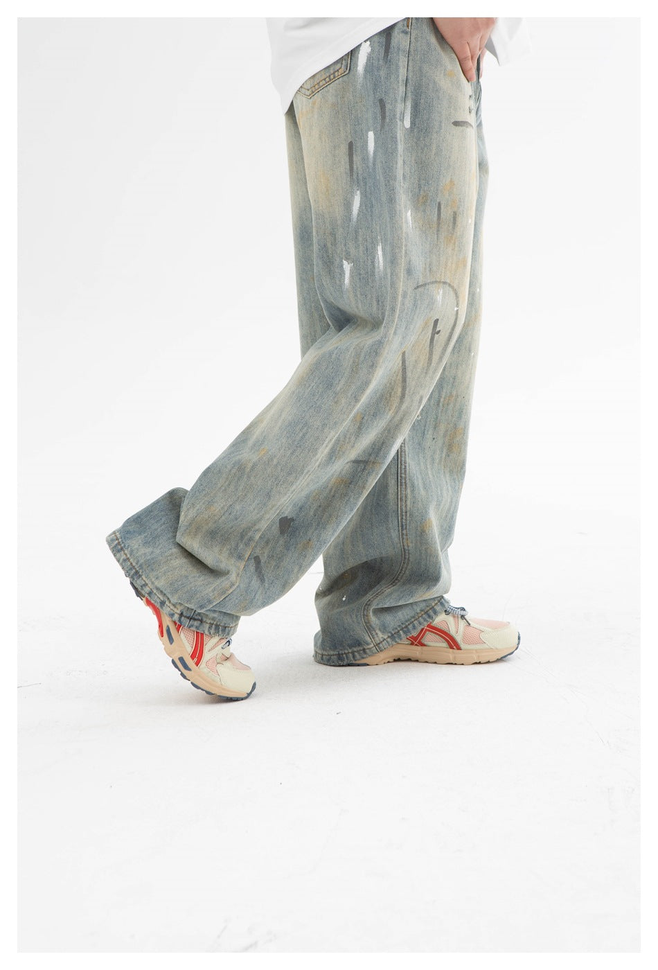 Side view of a person wearing loose, faded blue jeans with distressed paint-like marks and sneakers.