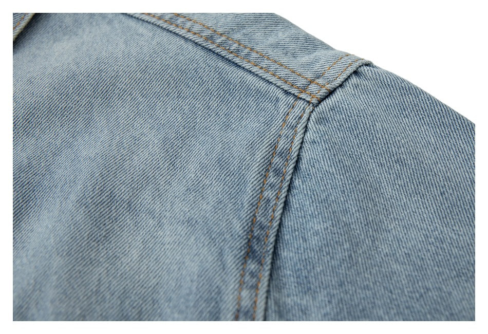 Close-up of a light blue denim jacket shoulder seam and tan stitching.