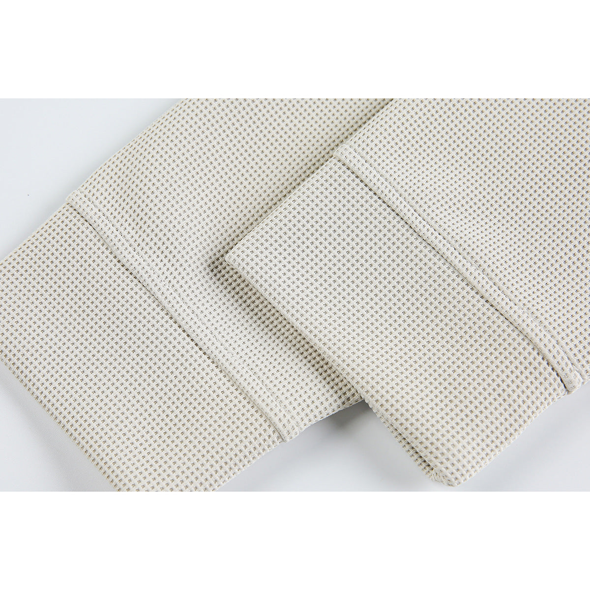 Close-up of ivory waffle-knit fabric with an overlapping stitched panel.