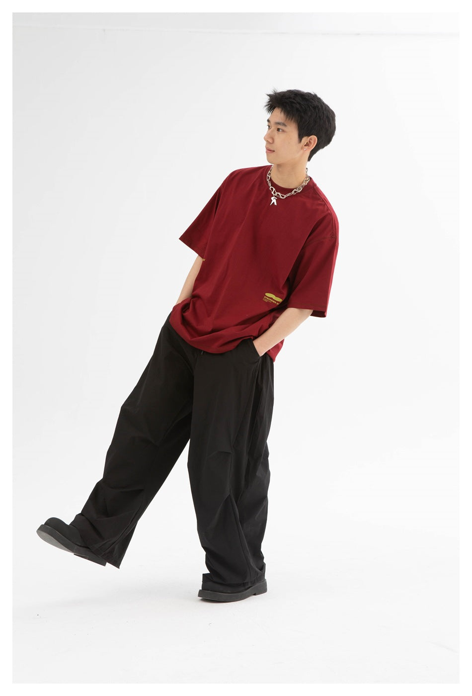 Model in a burgundy oversized T-shirt and loose black trousers, shown in a relaxed pose.