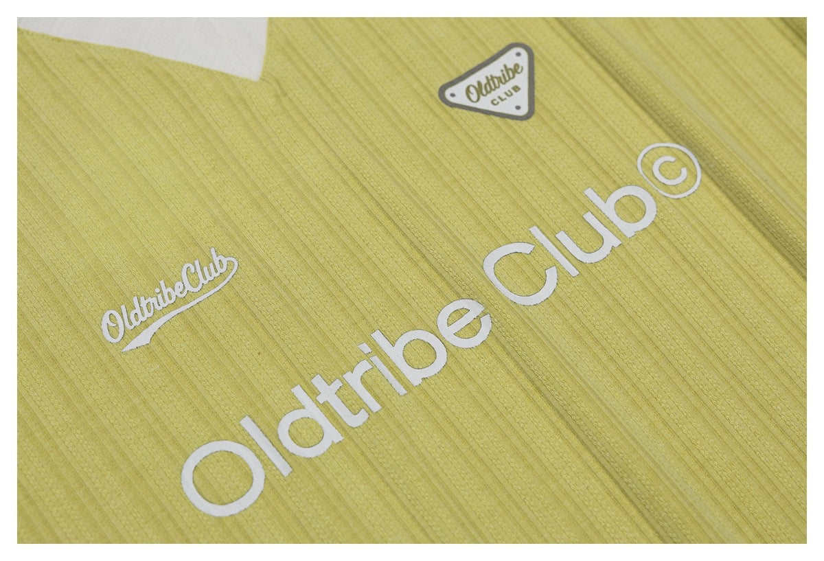 Close-up of pale yellow shirt fabric with white Oldtribe Club lettering and a small badge.