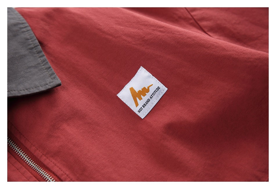Close-up of a small white-and-gold logo patch on the red jacket beside its charcoal collar and zipper.