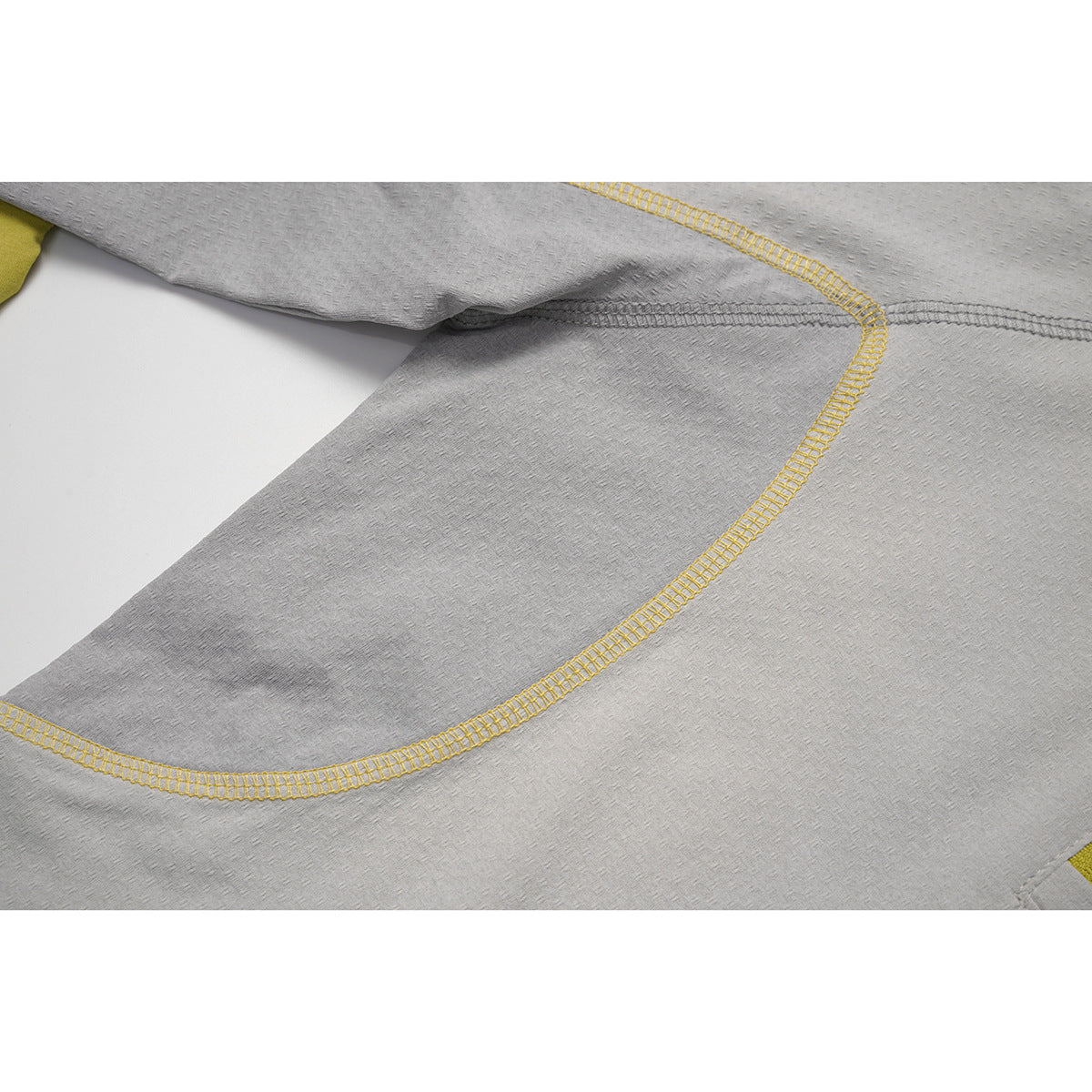 Close-up of curved yellow overlock stitching and seam details on a light gray top.