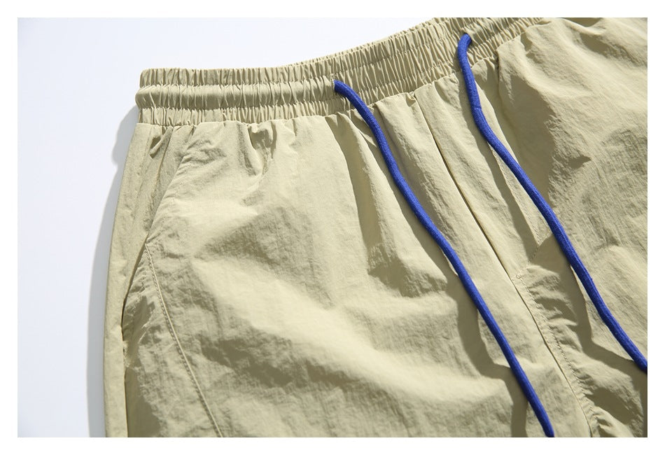 Close-up of the gathered elastic waistband and blue drawstrings on the pale khaki shorts.