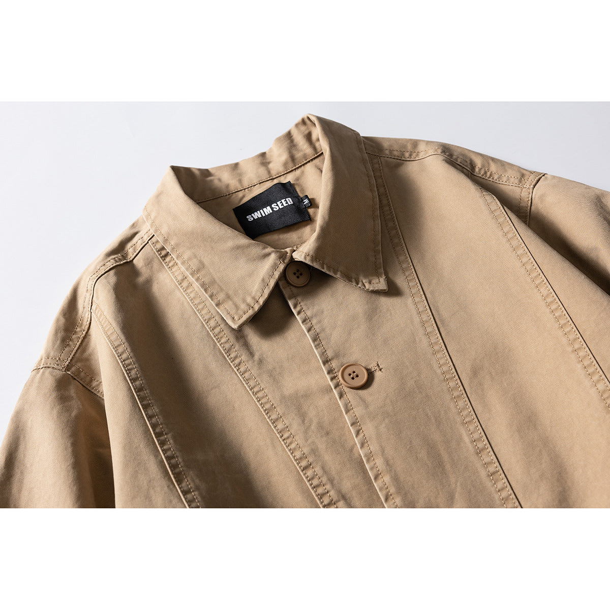 Close-up of a tan jacket collar, buttons, and stitched panels with a black neck label.