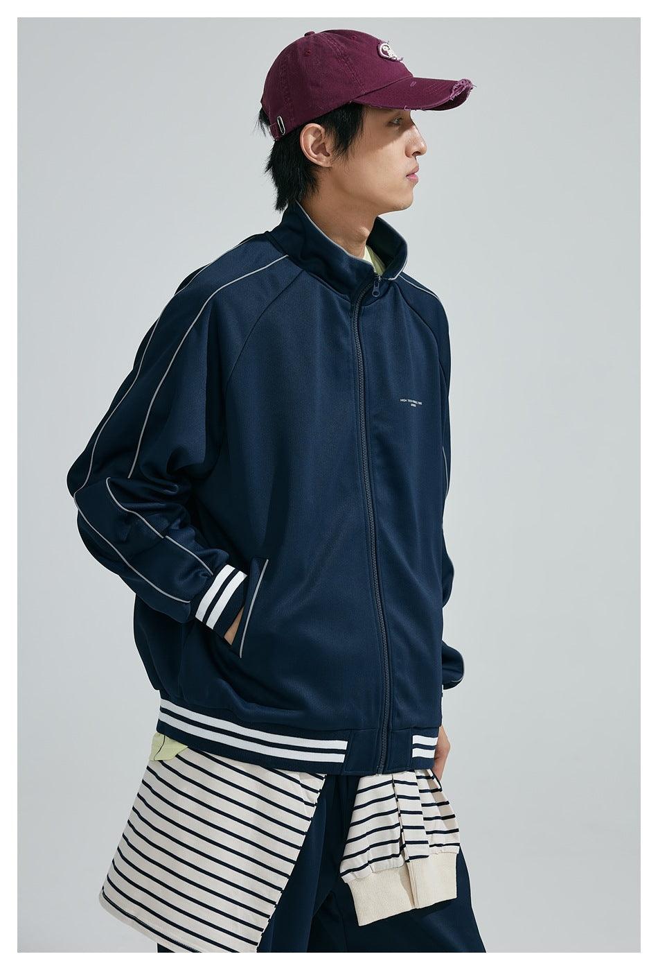 Model wearing a zipped navy track jacket with white piping and striped trim, shown at an angle.